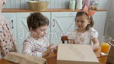 带礼盒的快乐孩子.. 早上，男孩和女孩打开盒子，厨房里放着糖果，家庭早餐快乐